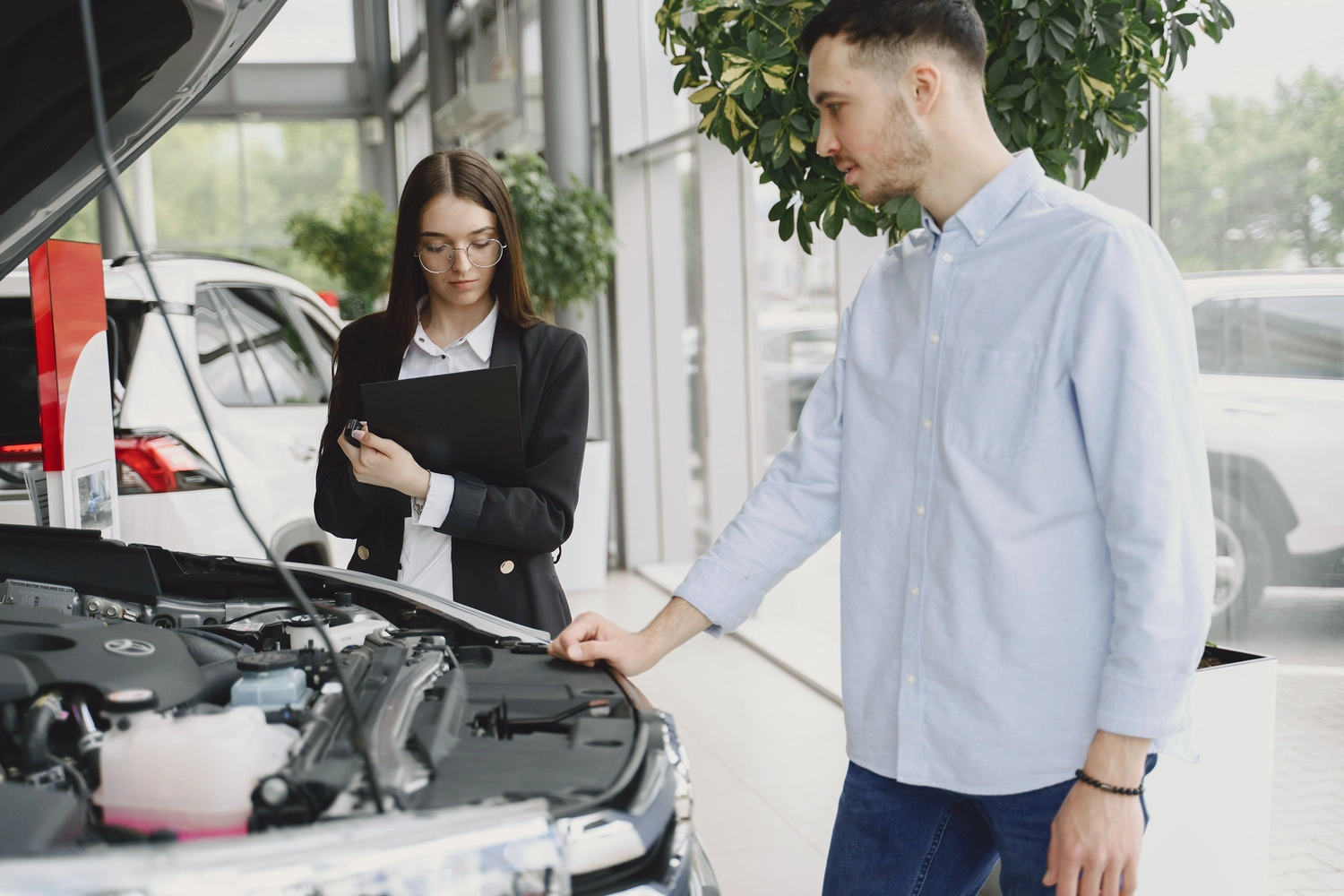 Stern Wagen GmbH -  Fahrzeug Einkauf - Ein Autoberater erklärt einem Kunden in einem Autohaus die Details des Motors.